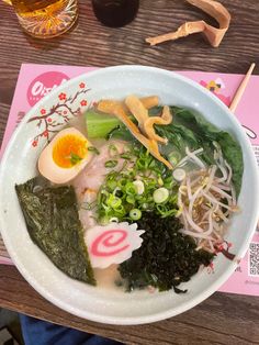 a white bowl filled with lots of food on top of a wooden table next to a drink