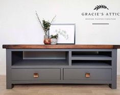 a gray entertainment center with drawers and a plant on it's top shelf, in front of a white wall