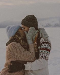 two people are kissing in the snow with one woman wearing a hat and scarf on her head