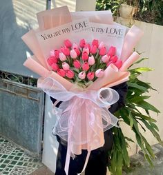 a man holding a bouquet of pink tulips in front of a sign that says you're my love