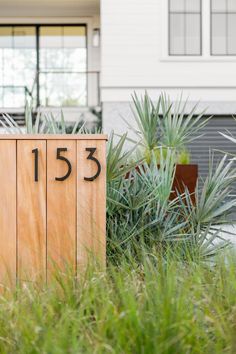 a wooden sign sitting in the grass next to a building with numbers printed on it