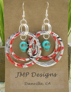 two pairs of earrings with red and white paper wrapped around them, on top of a cardboard box