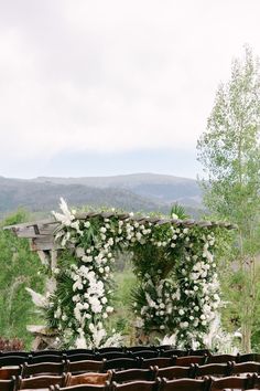 an outdoor ceremony setup with white flowers and greenery on the back of chairs in front of mountains