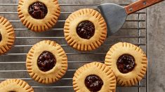 small pies with jam in them on a cooling rack next to a spatula