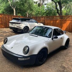 two white porsches parked next to each other in a parking lot near a wooden fence