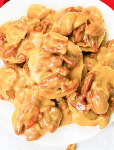 a white plate topped with dumplings covered in orange sauce and pecans next to a red table cloth