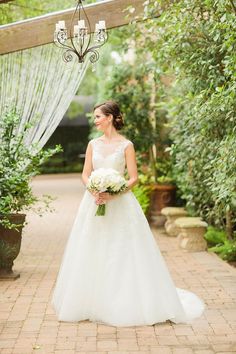 a woman in a wedding dress standing under a gazebo with flowers and greenery