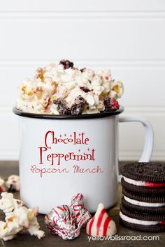 chocolate peppermint popcorn snack mix in a white mug surrounded by cookies and candy