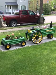 a green wagon with flowers in it sitting on the sidewalk next to a red truck