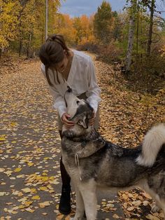 a woman petting a dog on the side of a road with leaves all over it