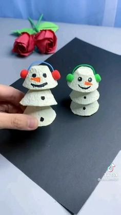 two snowmen made out of toilet paper sitting on top of a black piece of paper