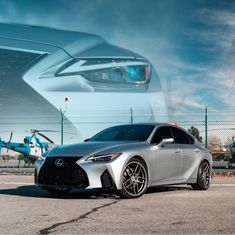 a silver sports car parked in front of a building with an airplane behind it on a sunny day