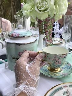 a table topped with plates and cups covered in lacy gauze next to a vase filled with flowers