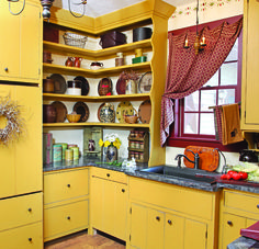 a kitchen with yellow cabinets and black counter tops is pictured in this image, there are dishes on the shelves