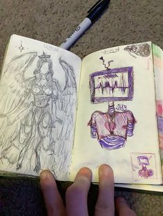 a hand is holding an open book with drawings on it and a pen next to it