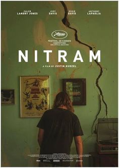 a man standing in front of a green wall with the words nitram on it