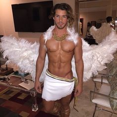 a shirtless man with white wings standing in a living room next to a table