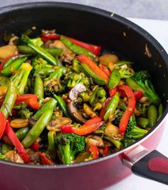 stir fry with broccoli, peppers and mushrooms in a red pan on the stove