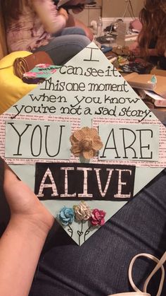 someone is holding up a graduation cap that says you are alive and has flowers on it