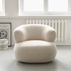 a white chair sitting in front of a window next to a radiator and books