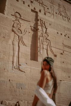 a woman standing in front of an egyptian wall