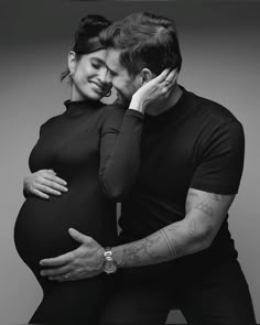 a black and white photo of a pregnant couple hugging each other with their hands on the belly