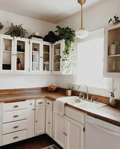 a kitchen with white cabinets and wooden counter tops, potted plants on the window sill