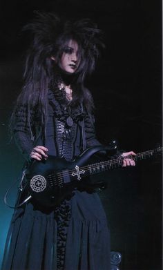 a woman with long hair is holding a guitar in her hands and wearing a black outfit