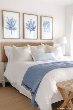 a bed with white and blue sheets in a bedroom next to two pictures on the wall