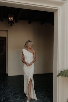 a woman standing in an open doorway wearing a white dress