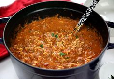 a pot filled with pasta and sauce on top of a stove next to a red towel