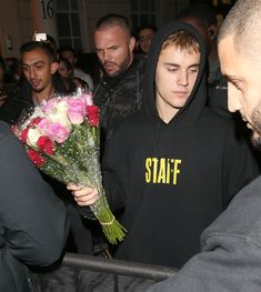 a man in a hoodie is holding flowers and looking at another man wearing a sweatshirt