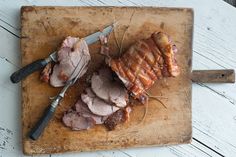 sliced meat sitting on top of a wooden cutting board next to knifes and fork