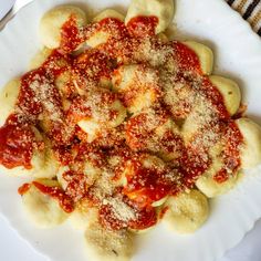 a white plate topped with ravioli covered in marinara sauce and parmesan cheese