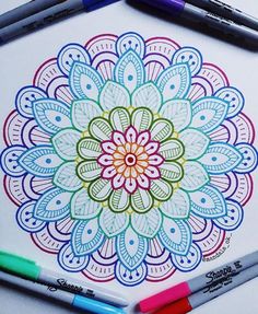 a coloring book with markers and pens on the table next to it is an image of a colorful flower