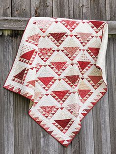 a red and white quilt hanging on the side of a wooden fence next to a piece of wood