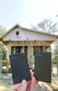 someone holding up two different color samples in front of a house