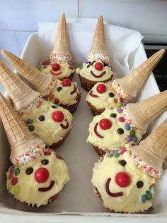 cupcakes decorated with ice cream and clown faces are arranged in a box on the table