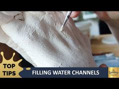 a person is working on something with white paint and a pen in their hand that reads top tips filling water channels