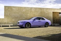 a purple rolls royce parked in front of a building with a stone wall behind it