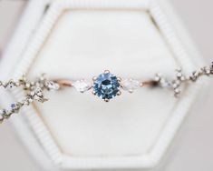 a blue diamond ring sitting on top of a white hexagonal box with flowers around it