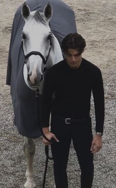 a man standing next to a horse with a blanket on it's head and holding the reins