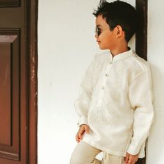 a young boy standing against a wall with his hands in his pockets and looking down