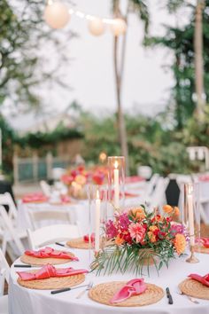 the table is set with place settings and flowers on it, along with candles for centerpieces