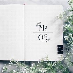 an open notebook sitting on top of a table next to white flowers and greenery