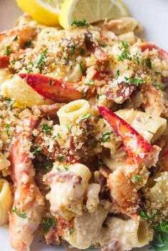 a white plate topped with pasta covered in shrimp and sauce next to a lemon wedge