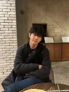 a young man sitting at a table with his arms crossed and looking into the camera