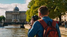 a man with a backpack is taking a photo by the water in front of a building