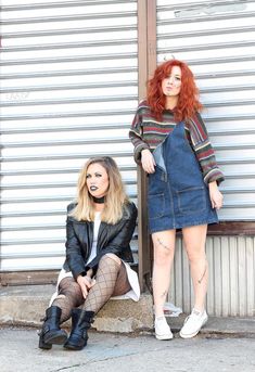 two women sitting next to each other in front of a metal door with their legs crossed