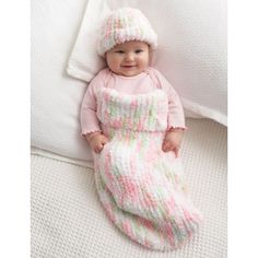 a baby wearing a pink and green knitted outfit laying on top of a bed